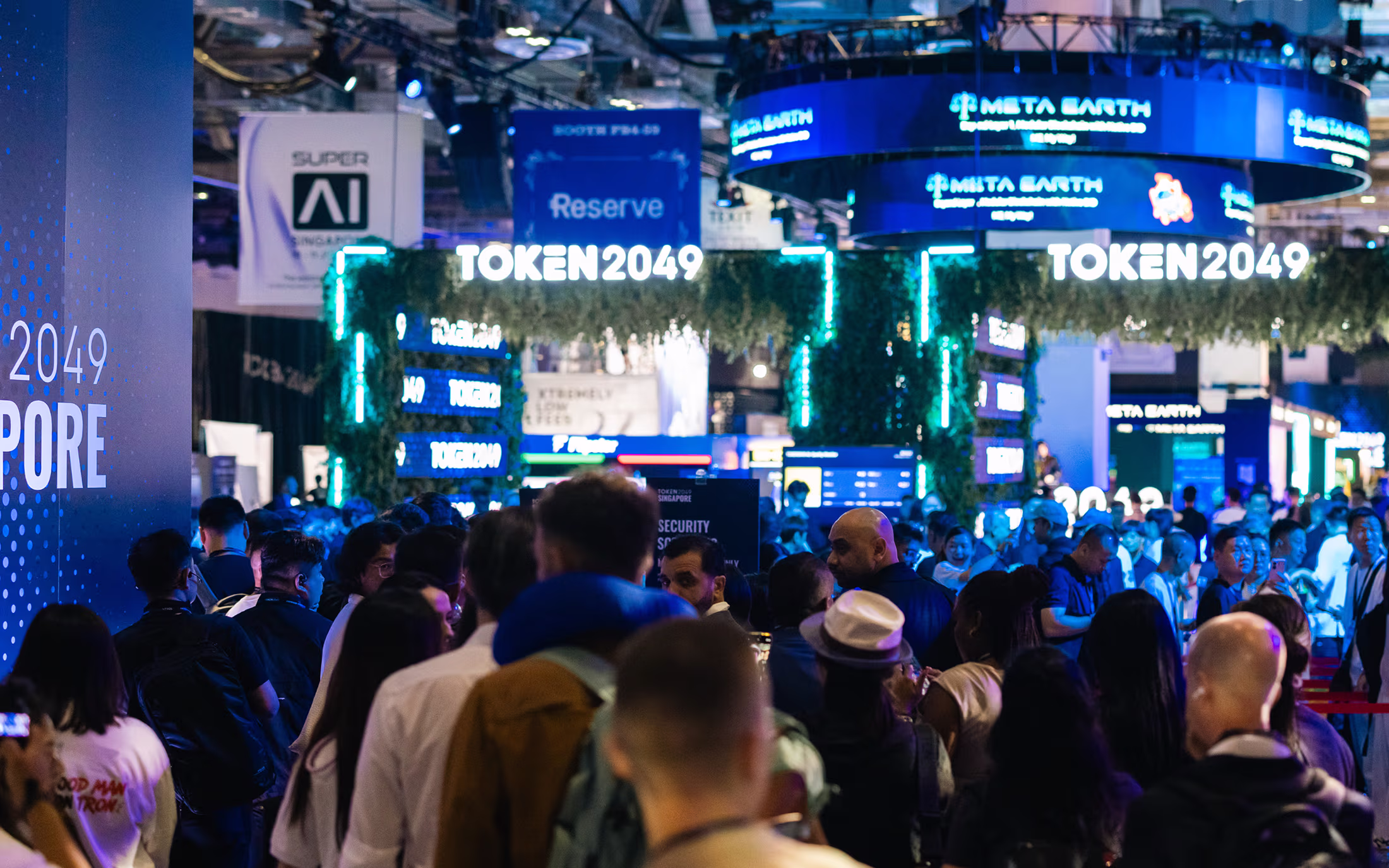 Crowded event hall with illuminated TOKEN2049 signage and various booths at a technology conference in Singapore.